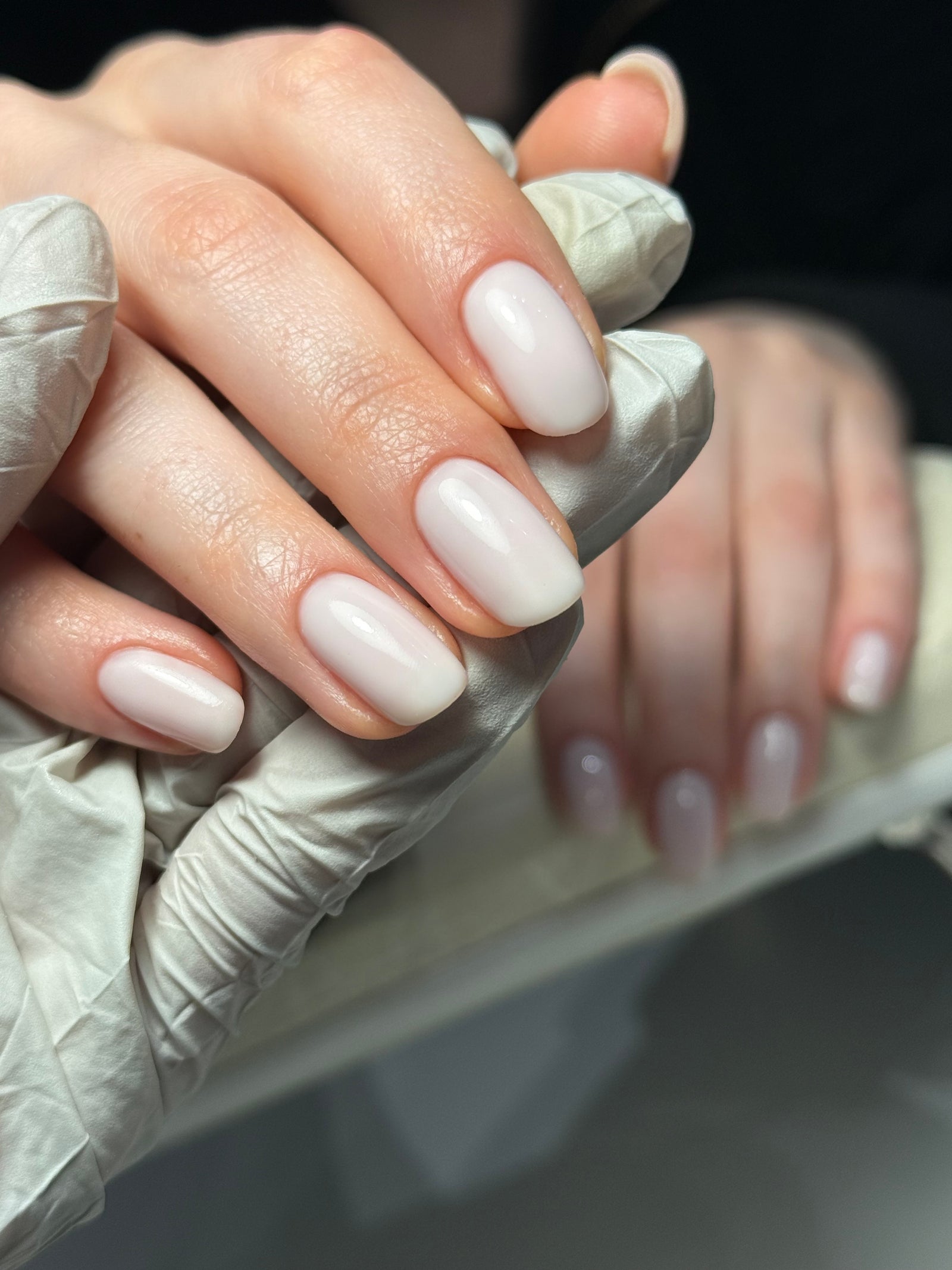 Melkwitte gellak op korte, ovale nagels, de hand rust op de handsteun van de lamp