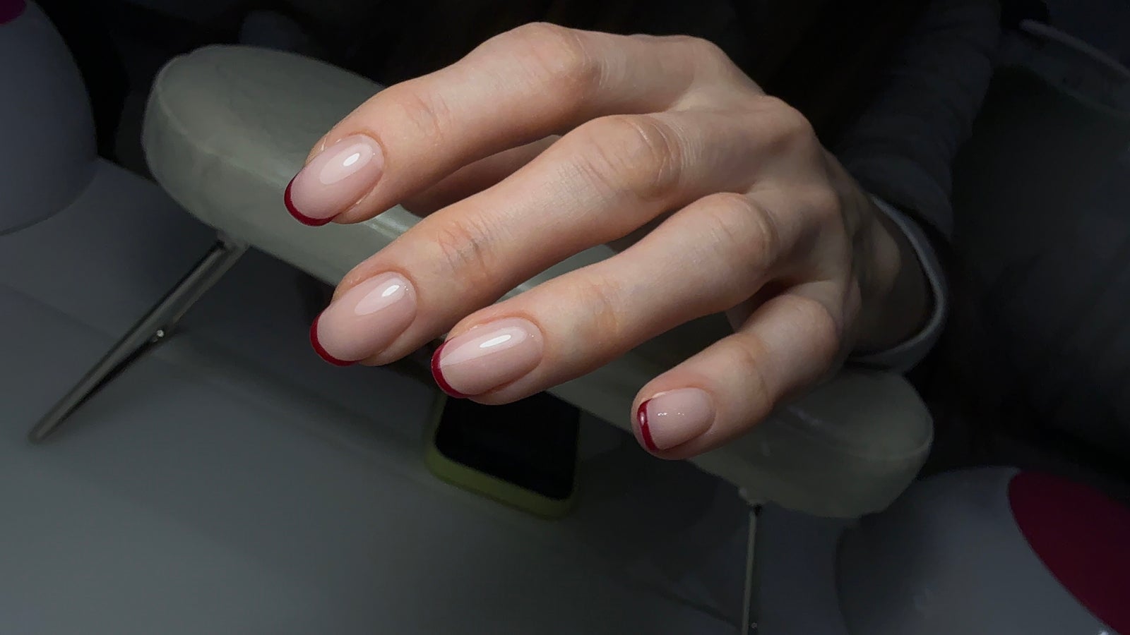 Nude nagels met donkerrode puntjes, de hand rust op de handsteun van de lamp